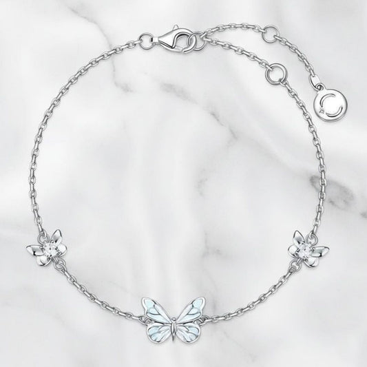 Pulsera de mariposa y flores en tono plateado sobre mármol blanco